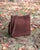 Le sac Mini Étrivière Renouard en cuir veau velours acajou et sa bandoulière cuir, vu en ambiance.