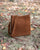 Le sac Mini Étrivière Renouard en cuir veau velours noisette et sa bandoulière cuir, vu de quart en ambiance.