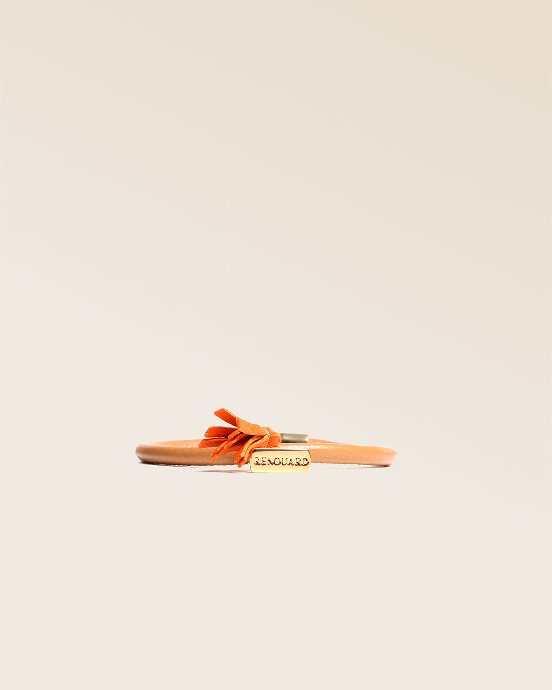 Notre bracelet Jumping Renouard en cuir d'agneau camel et pompon orange, vu de face en studio.