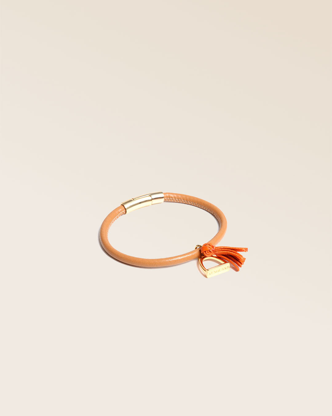 Notre bracelet Jumping Renouard en cuir d'agneau camel et pompon orange, vu de quart en studio.