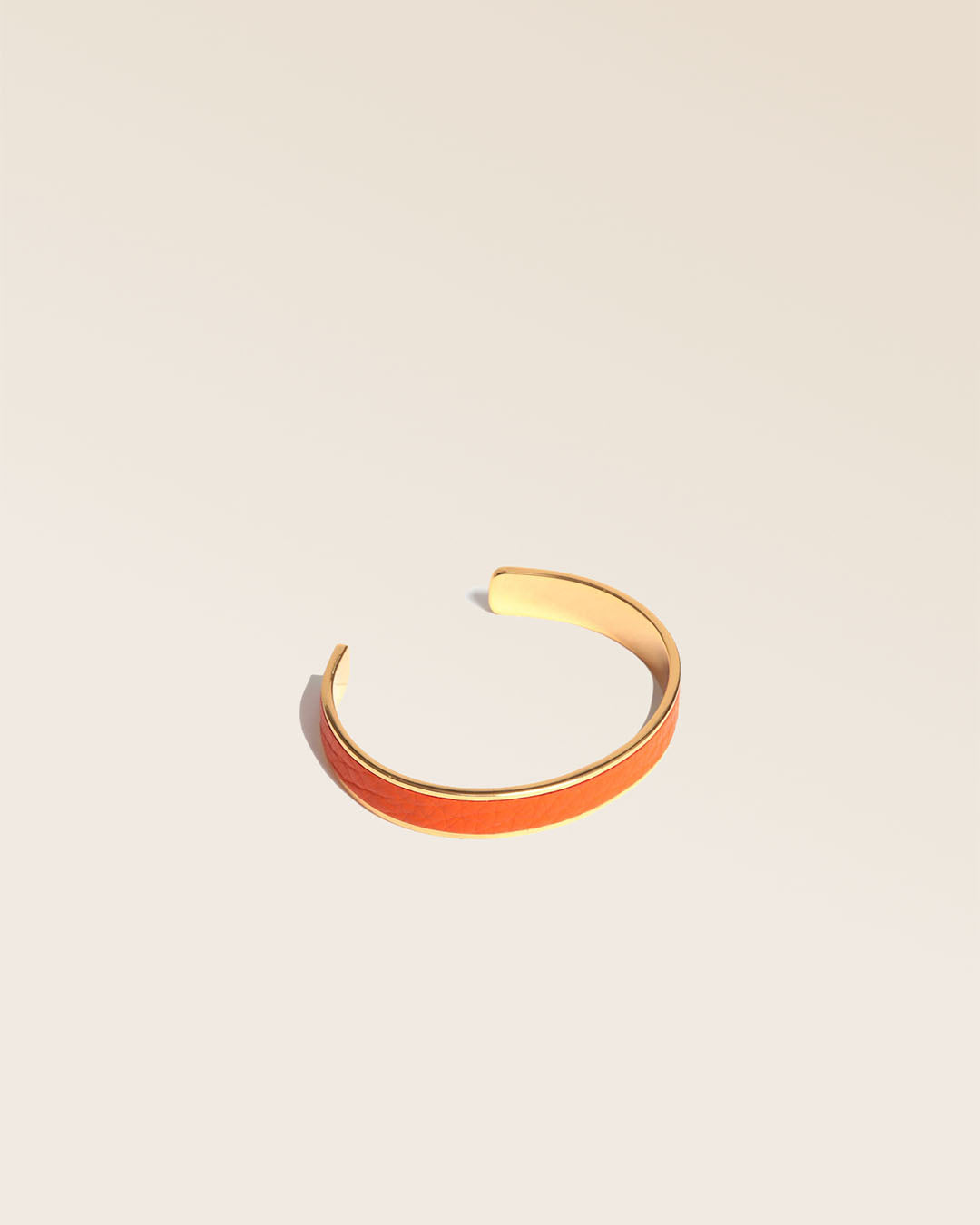 Notre bracelet Pacôme doré en cuir façon vigogne orange vu de quart en studio.