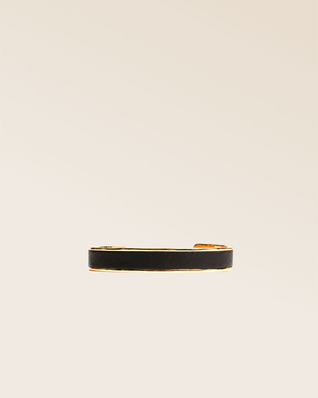 Notre bracelet Pacôme Renouard en métail doré et cuir lisse noir, vu de face en studio.