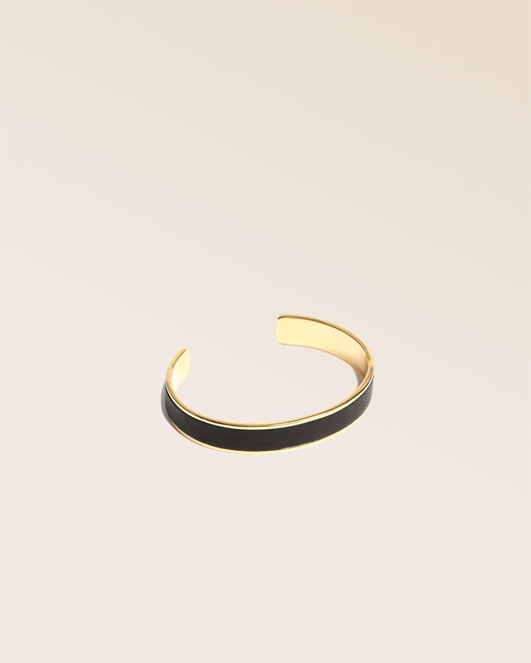 Notre bracelet Pacôme Renouard en métail doré et cuir lisse noir, vu de quart en studio.