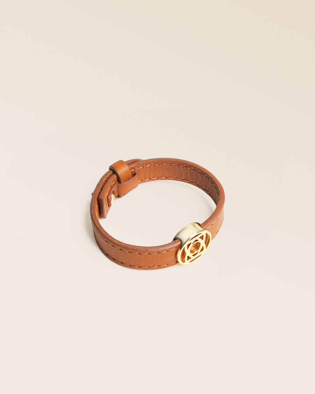 Le bracelet Alezan Renouard en cuir lisse camel et son accessoire doré, vu de quart en studio. 