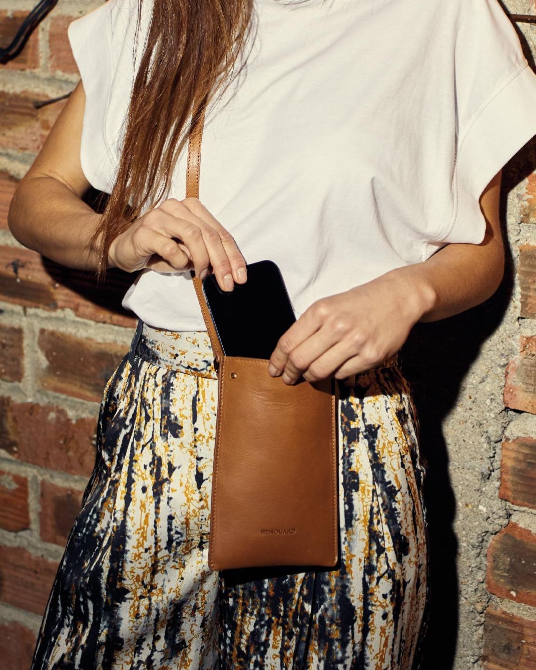 Notre pochette téléphone Renouard en cuir vintage camel vue portée par notre mannequin. 